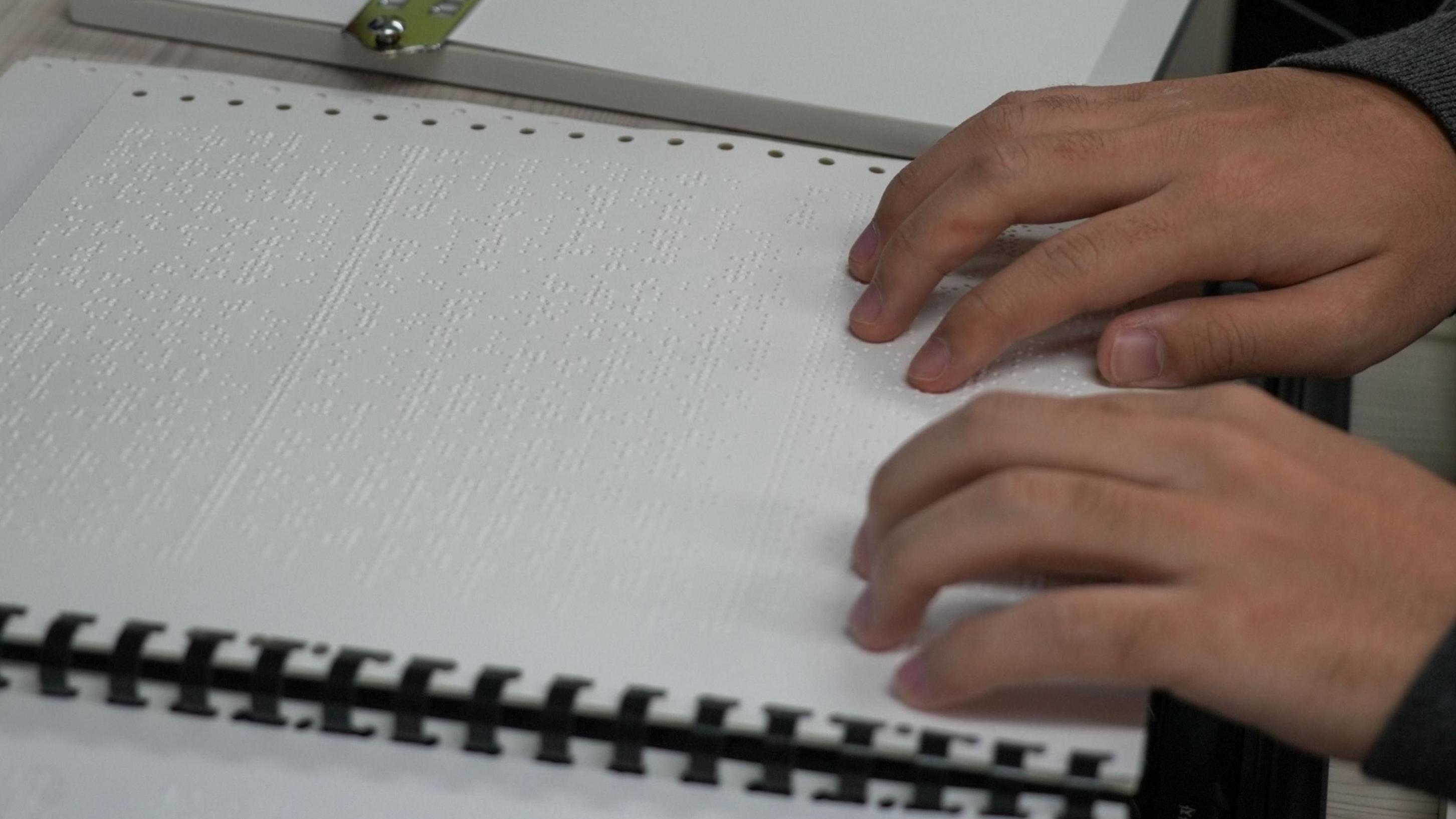 يدان على كُتيّب تدريب بطريقة برايل