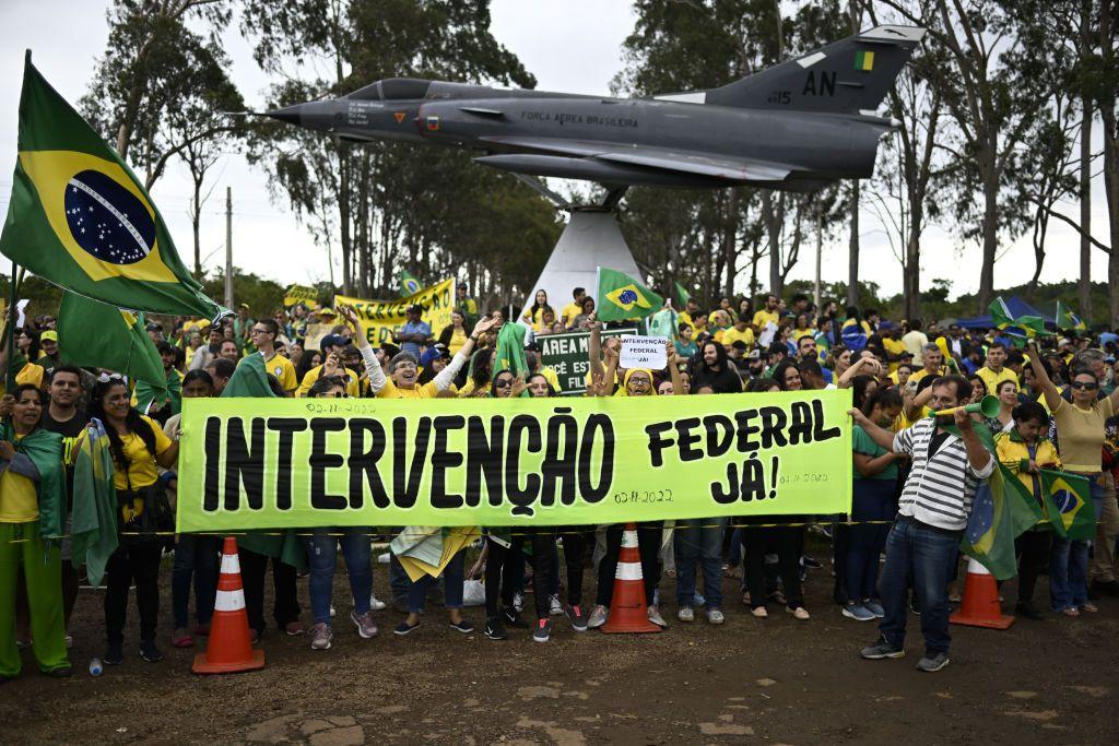 Seguidores del derrotado Bolsonaro reunidos en una zona militar de Brasilia tras el triunfo electoral de Lula en 2022, con banderas de Brasil y un cartel que pide una "¡Intervención federal ya!". 