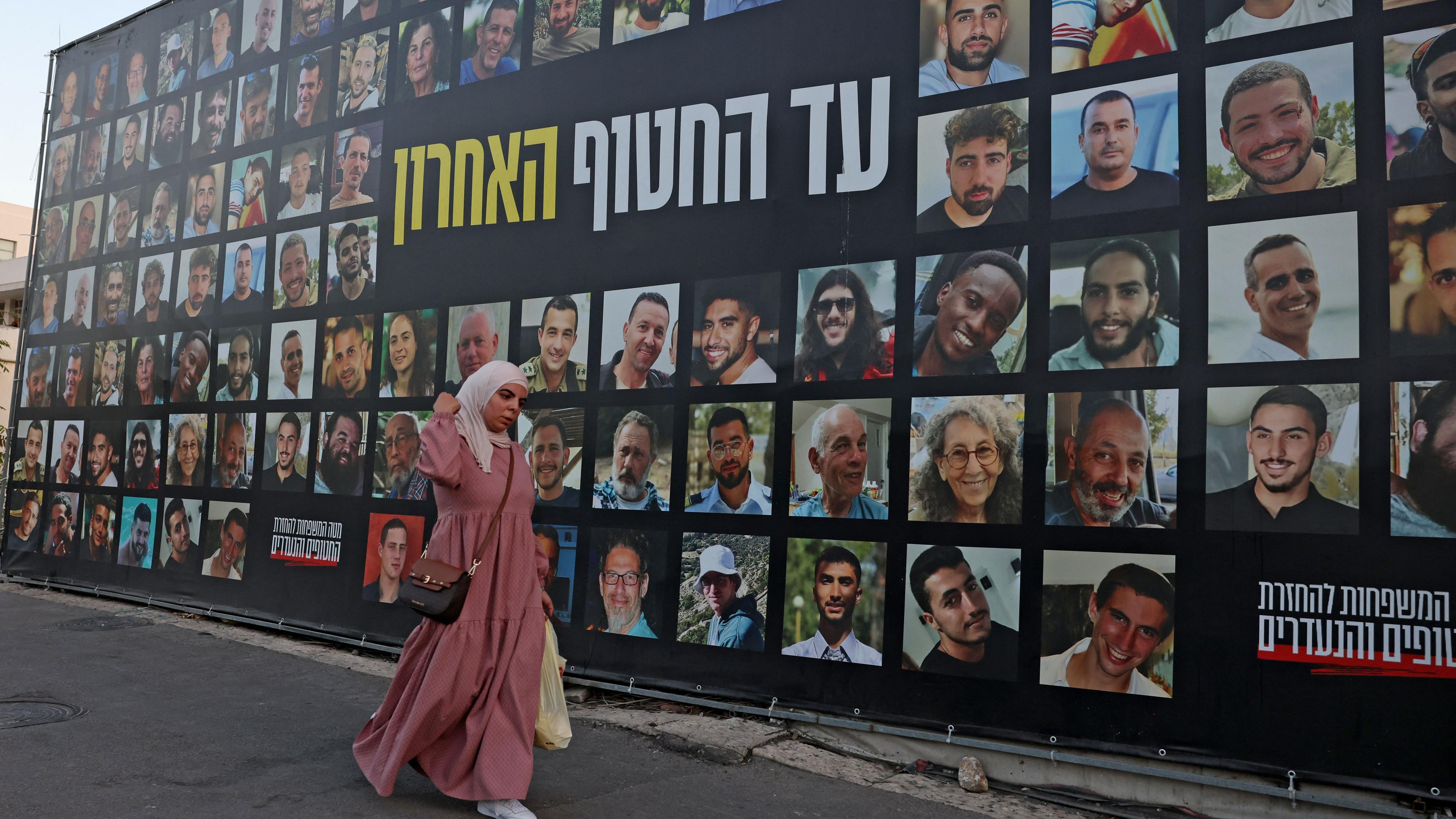 امرأة تمر أمام لوحة إعلانية تحمل صوراً لإسرائيليين محتجزين رهائن في قطاع غزة لدى مسلحين فلسطينيين منذ عام 2923، في القدس، 6 أكتوبر/تشرين الأول 2025. 