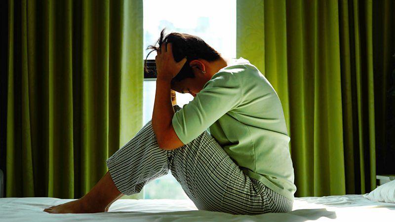 Mulher com as mãos na cabeça, sentada sobre uma cama