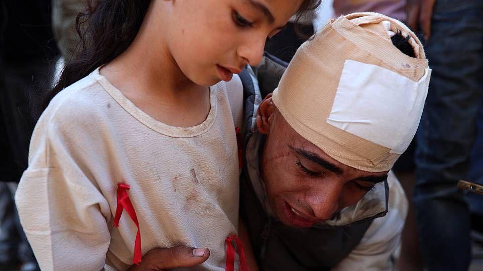 El esposo de Shaima Al-Shawish, con la cabeza vendada, llora abrazando a su hija de unos 10 años mientras observa los restos de su mujer. 