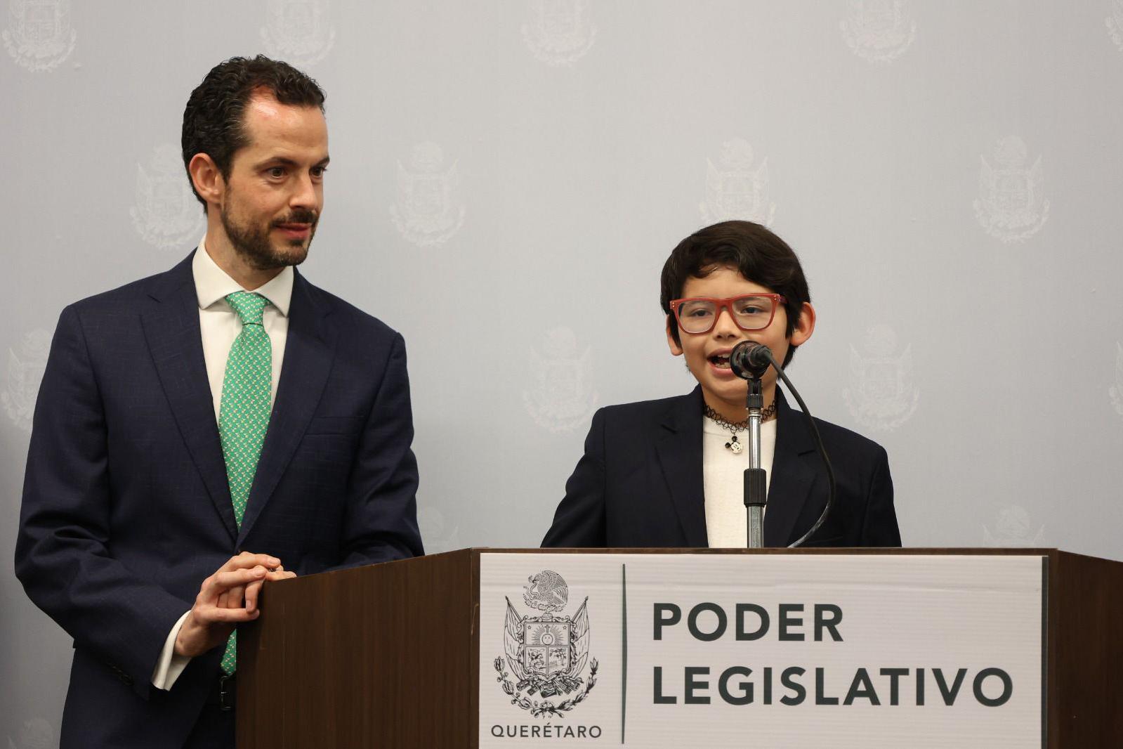 David Camacho, acompanhado por um adulto, de p&eacute; em frente a um p&oacute;dio e falando ao microfone, durante uma confer&ecirc;ncia promovida pelo governo local de Quer&eacute;taro, no M&eacute;xico