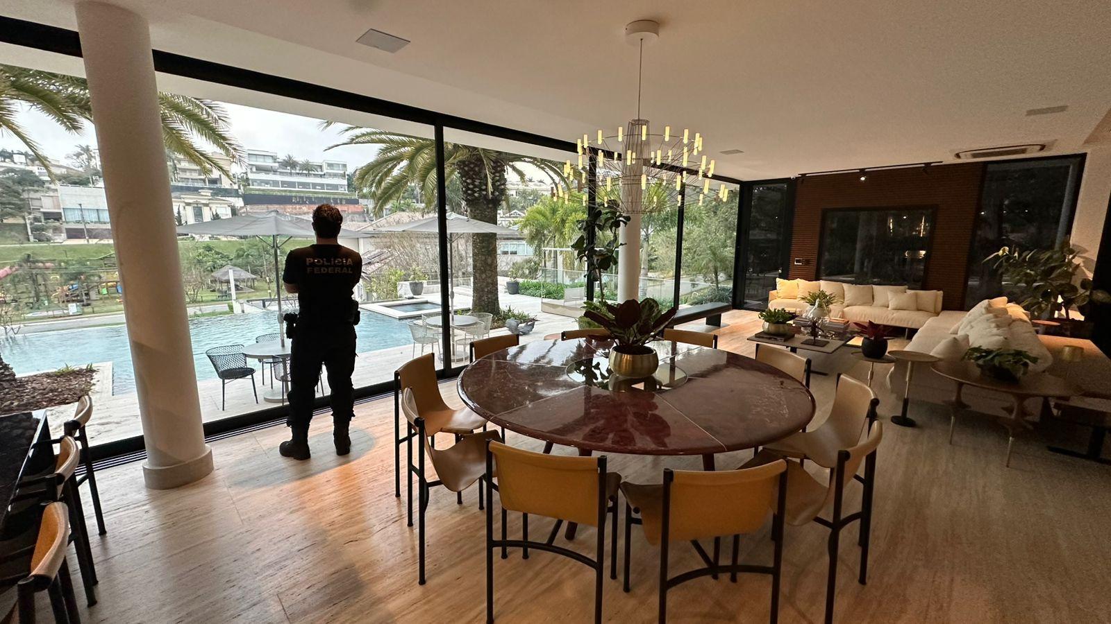 Agente da polícia federal está de costas em sala de jantar de casa de luxo alvo da operação contra lavagem de dinheiro em postos de combustíveis