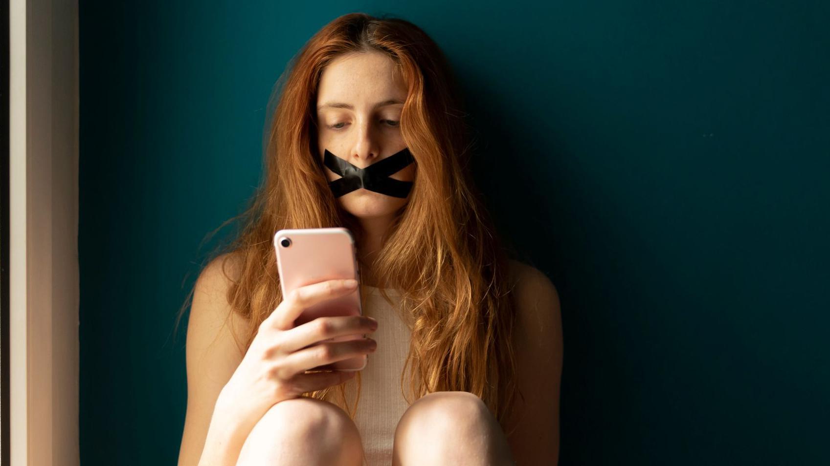 Una mujer joven con la boca tapada usando un teléfono móvil.