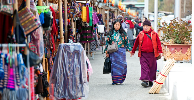 رجل وسيدة من السكان المحليين في مملكة بوتان داخل سوق به ملابس ملونة ومزركشة.