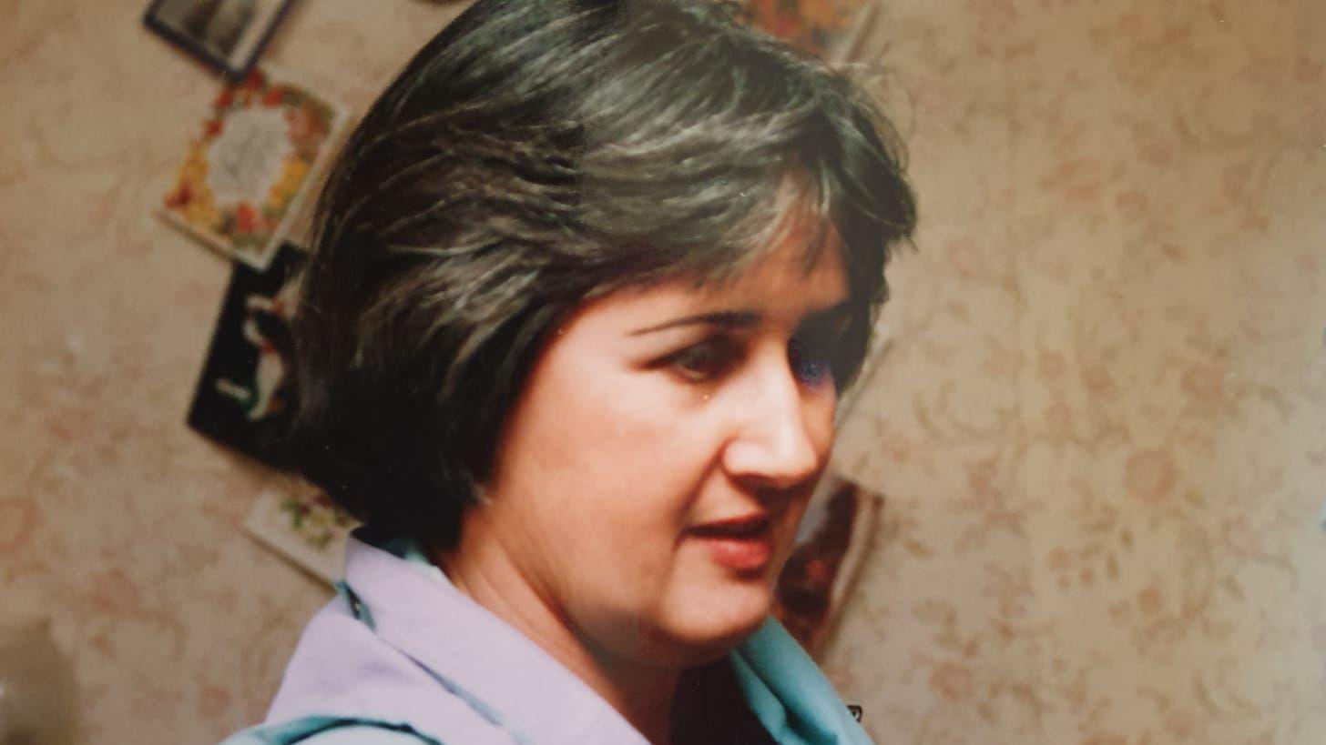 Archive side profile photograph of Judith Rhead. She has brown short hair, fringed at the front. Behind her a wall covered in cards can be seen. She has brown eyes.