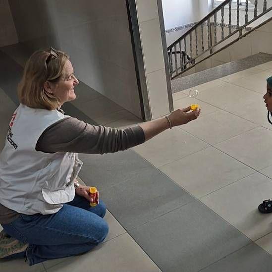 Katrin con el brazo extendido hacia una niña en el hospital Nasser, intentado atraer su atención con burbujas de jabón
