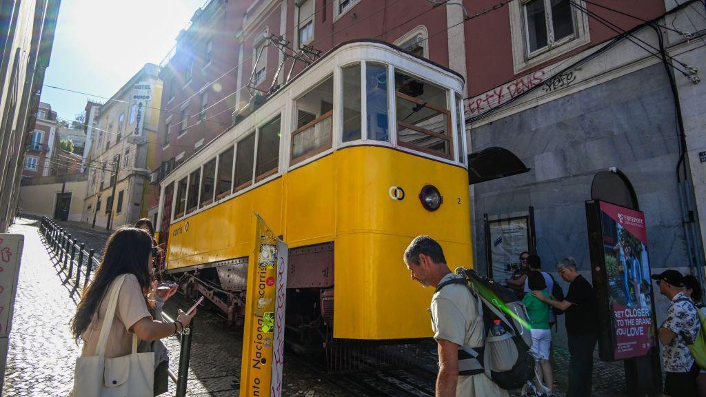 Un funicular de color amarillo y blanco subiendo una calle empinada en Lisboa.