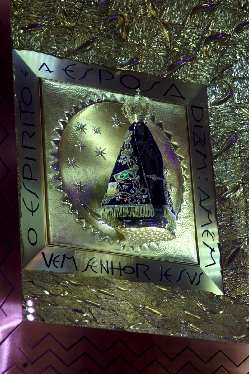 A imagem da santa de cor negra, vestindo seu manto azul bordado e coroa dourada, cercada de ornamentos também dourados