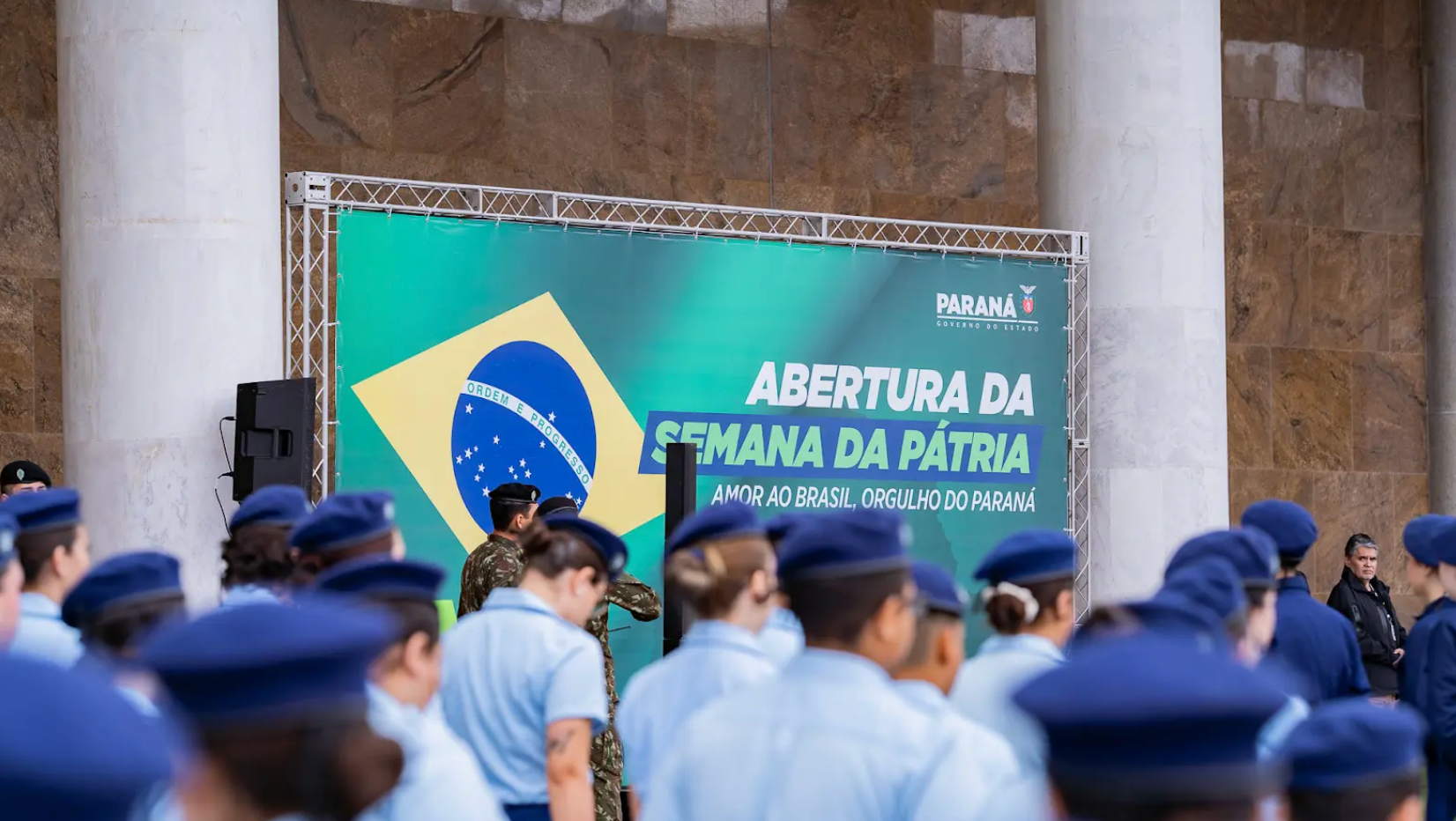 Estudantes em escola cívico-militar no Paraná, com placa ao fundo que contém bandeira do Brasil e dizeres 