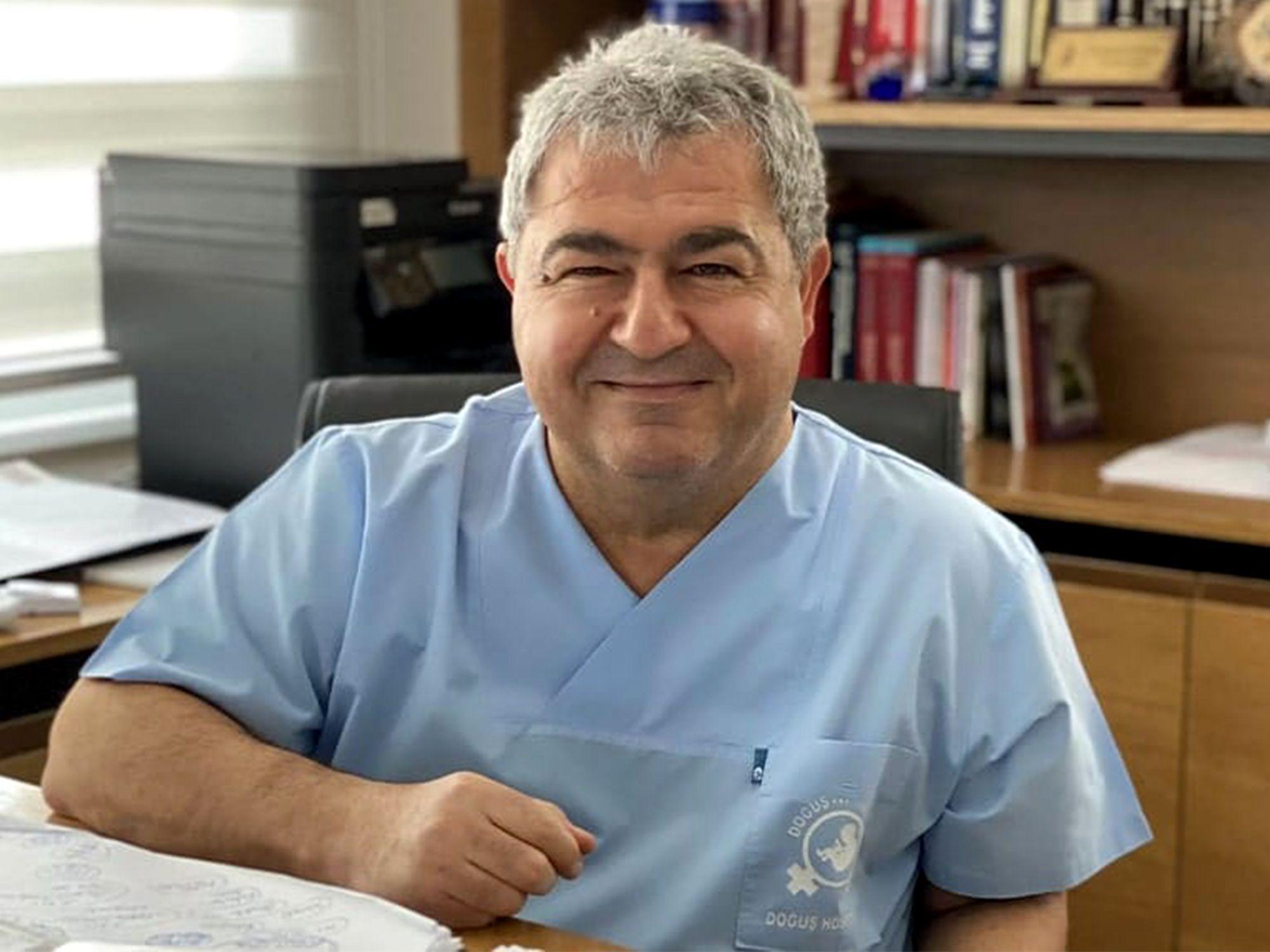 يرتدي الدكتور شوكت ألبترك زياً طبياً أزرق اللون ويجلس على مكتب، وشعره قصير رمادي اللون.
