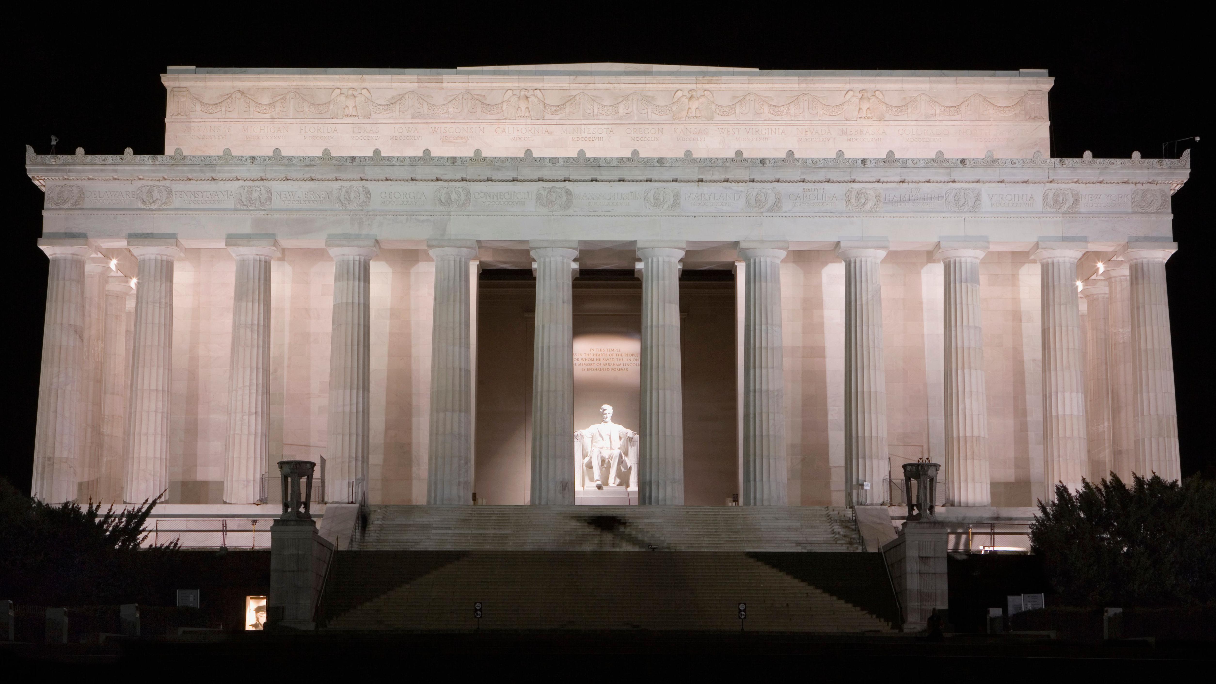 El Monumento a Lincoln iluminado por la noche. Se puede ver una gran estatua del expresidente estadounidense Abraham Lincoln iluminada entre las columnas del gran edificio en el que se encuentra la estatua.
