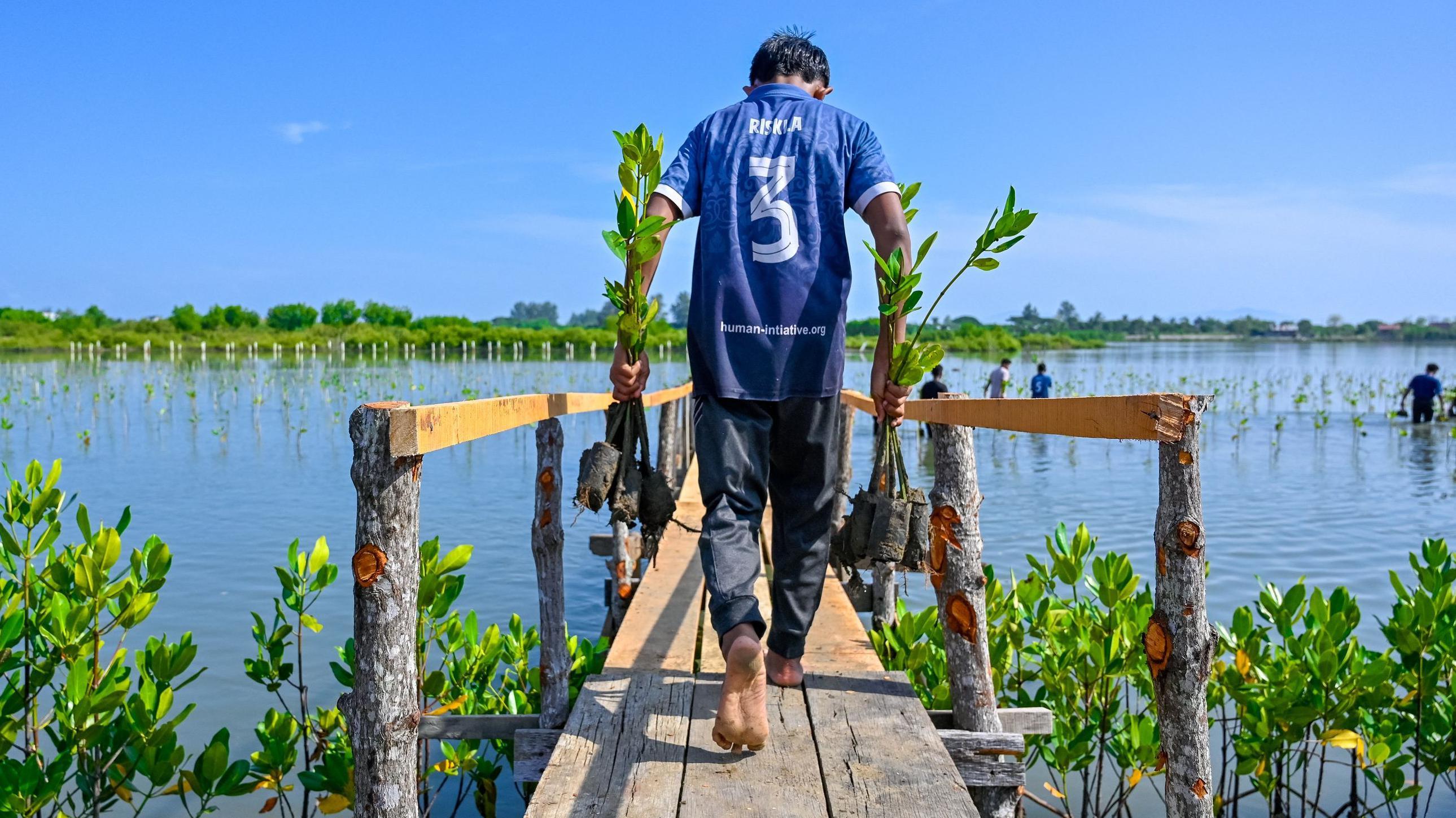 Un hombre con camiseta azul y pantalón oscuro camina por un paseo marítimo hacia el mar.