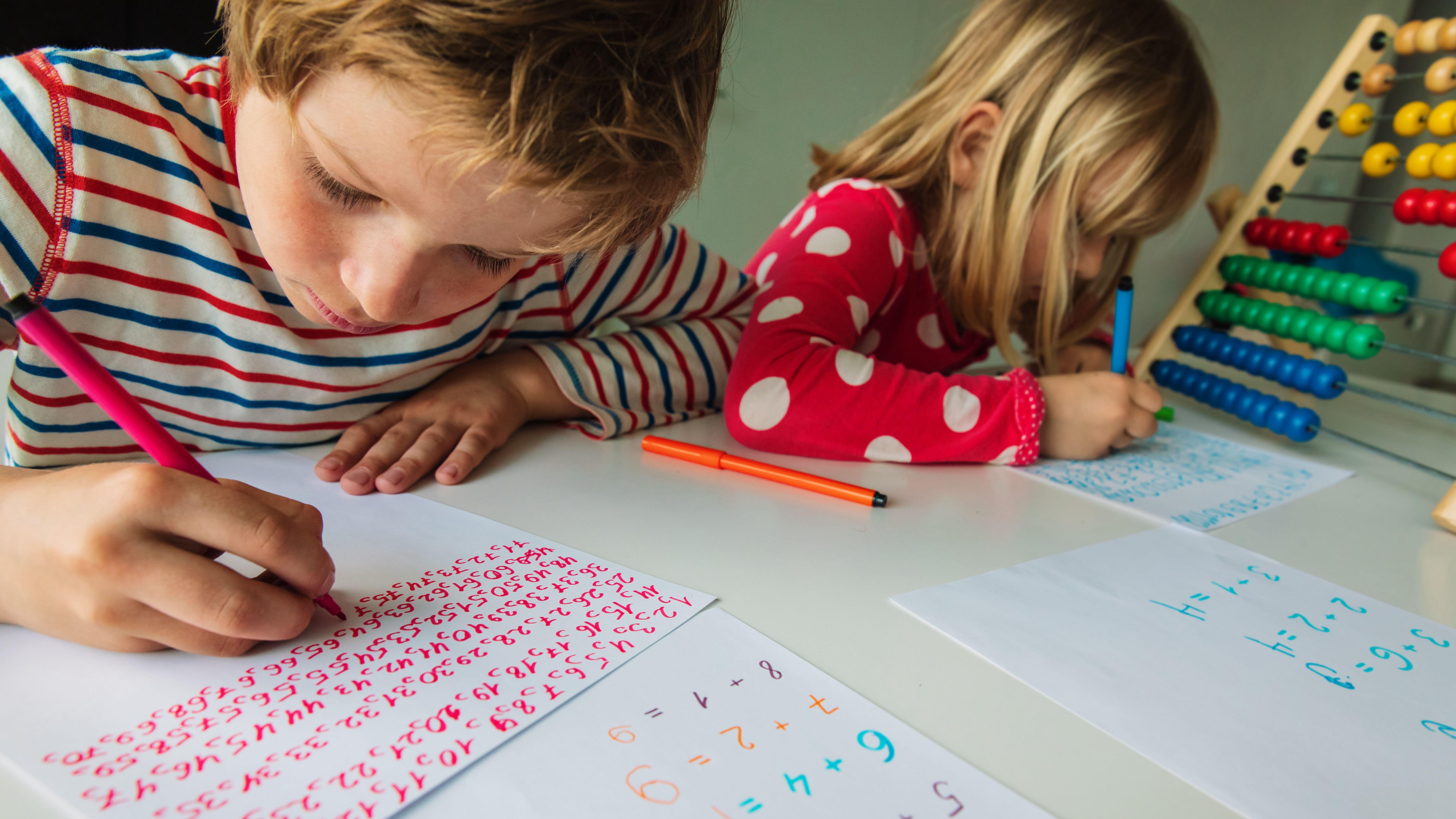 한 소년과 소녀가 책상에 나란히 앉아 색색의 펜으로 종이에 글을 쓰고 있다.