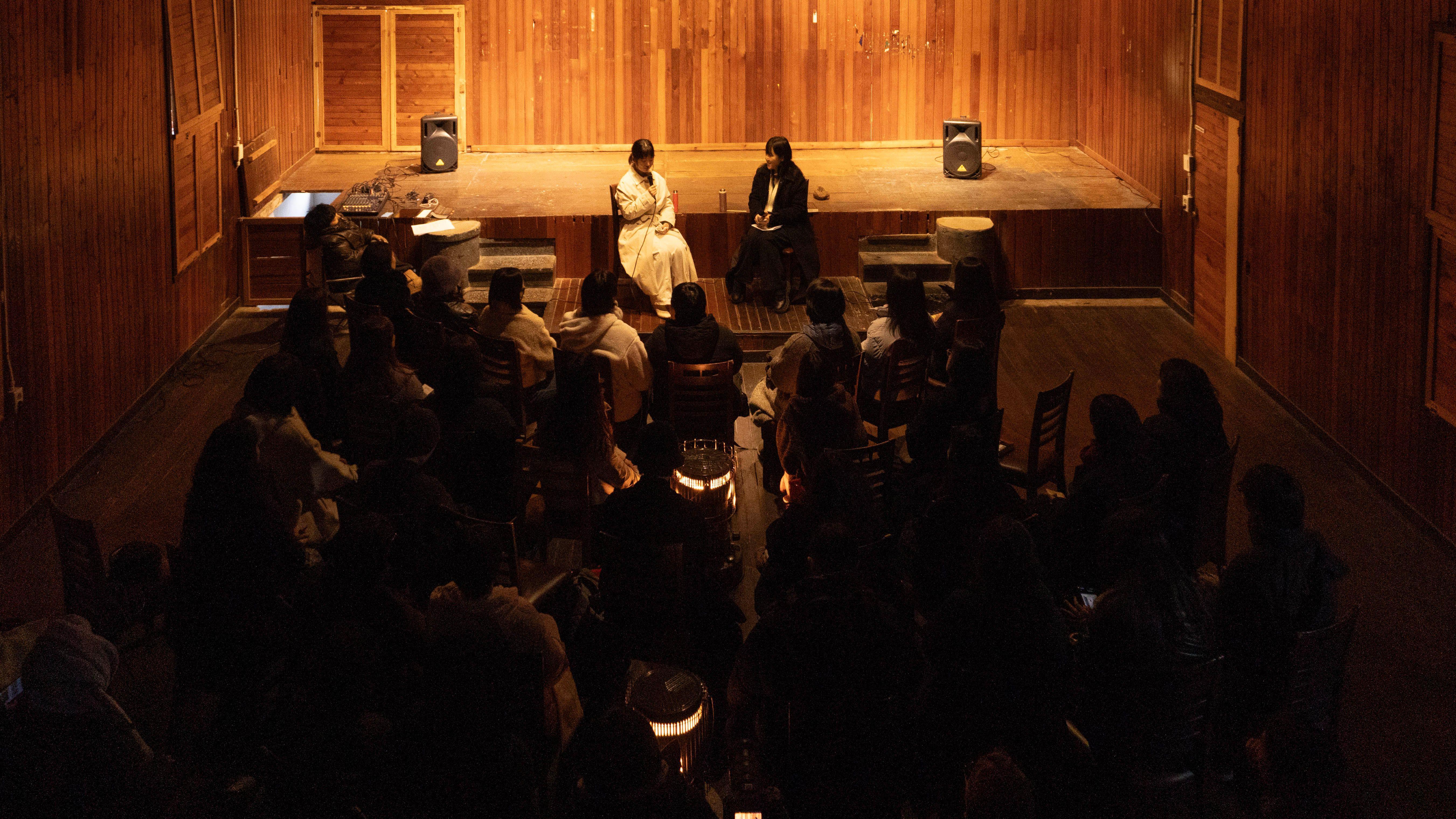 좁은 공간에서 여성 2명의 글 낭독을 경청하는 소수의 청중들