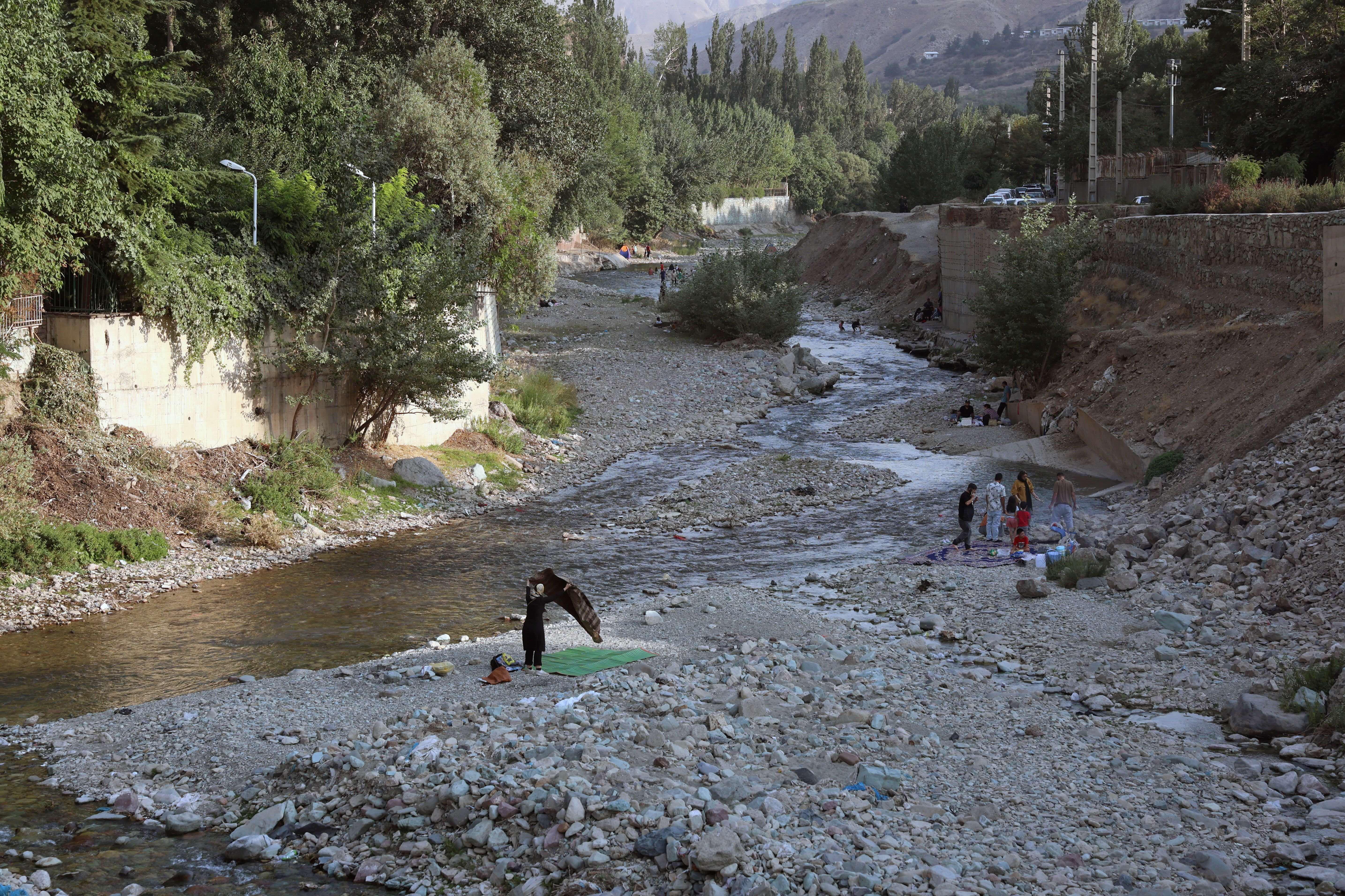 Iranianos passeiam pelo leito seco de um rio em Fasham, colocando uma esteira sobre as pedras
