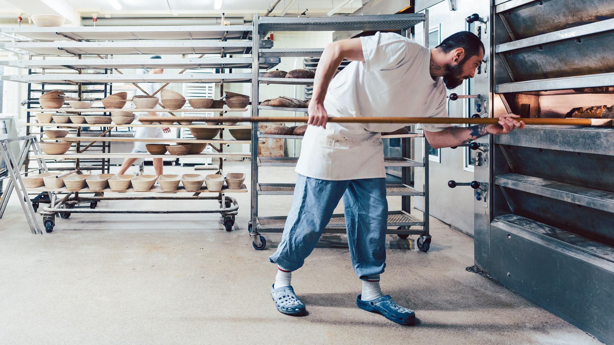 Un trabajador en una panadería de Alemania saca panes de un horno con una pala de madera