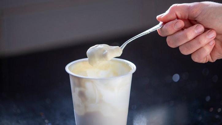 Foto de um pote branco de iogurte, com uma colher