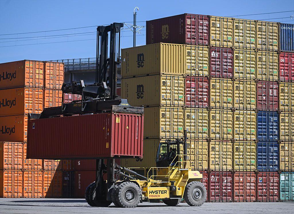Una grúa transportando un contenedor en un puerto lleno de contenedores de carga.