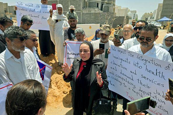 سيدة تخاطب مجموعة من المتظاهرين الذين حملوا لافتات كتب على إحداها:
 "We reject the integration of immigrants into health education and services and  demand their ... compulsory deportation"