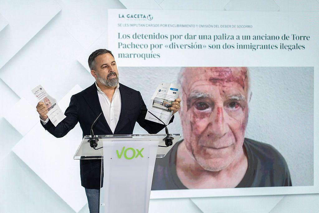El líder de Vox, Santiago Abascal, en una rueda de prensa con la imagen del anciano agredido de fondo.