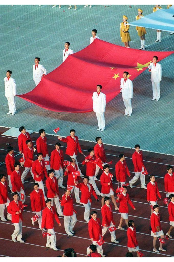 1997年10月12日第八屆全國運動會開幕式上，香港運動員手持小型區旗走過手持中國國旗的工作人員