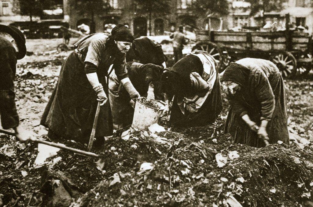Un grupo de mujeres con cubos y azadas agachadas sobre un montón de basura en una foto de época. 