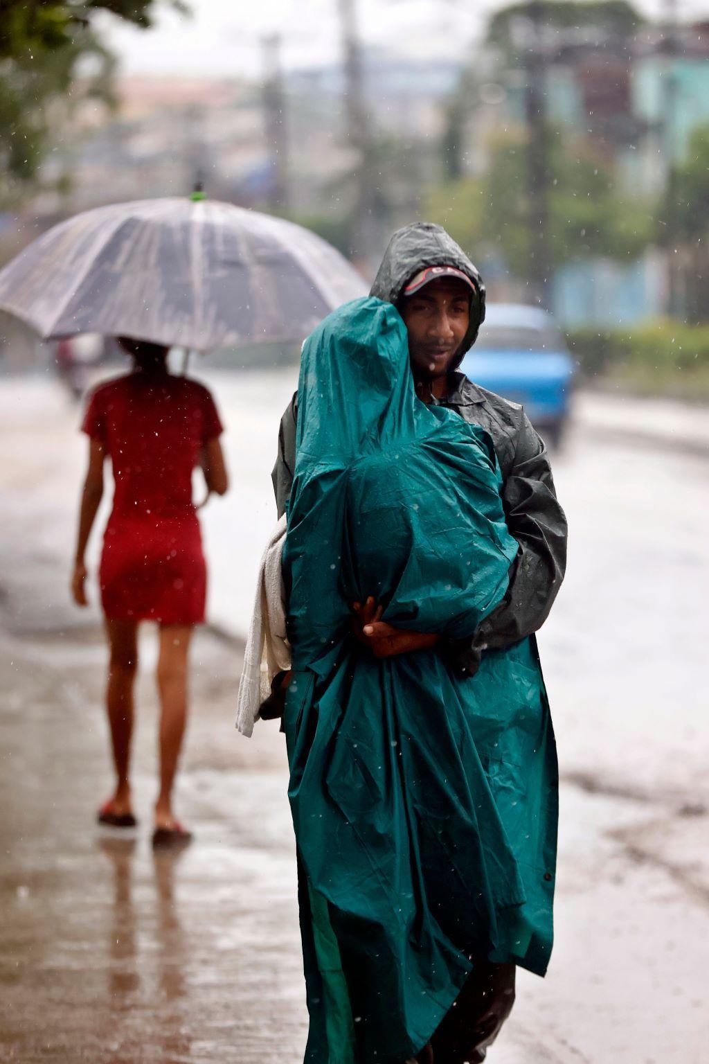 muškarac nosi dete dok pada kiše, oboje su u kabanicama, uragan, uragan melisa