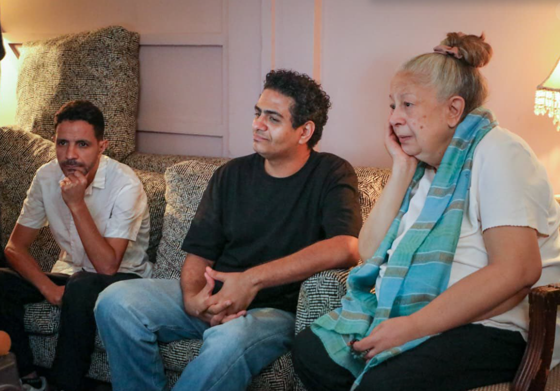 الفنانة سمية الألفي تجلس غلى أريكة في موقع تصوير فيلم" سفاح التجمع"، واضعةً يدها على أحد خديها وترتدي قميصاً ذا أكمام قصيرة، وسروالاًً أسود، ويجلس على يمينها رجلان، أحدهما هو مخرج ومؤلف الفيلم محمد صلاح العزب.