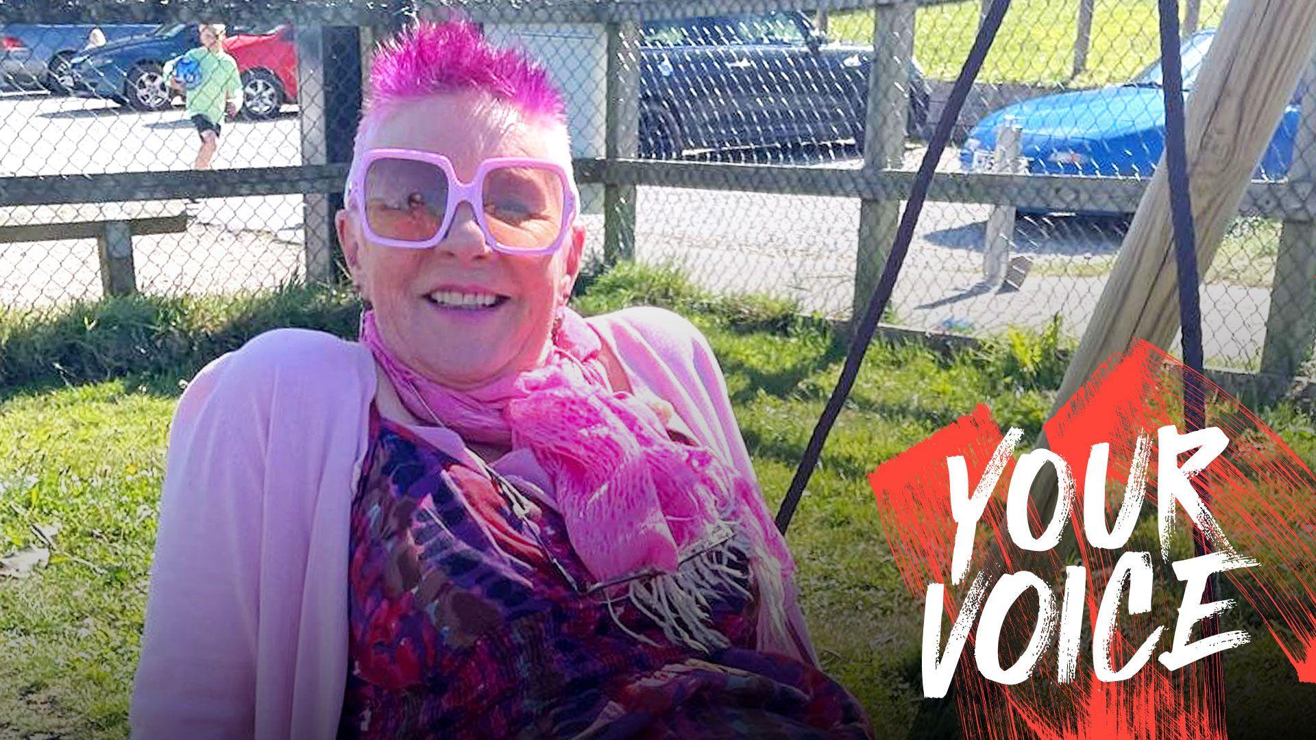 Annie Haslam, com cabelo curto espetado rosa, &oacute;culos rosa, cachecol rosa e cardig&atilde; rosa.