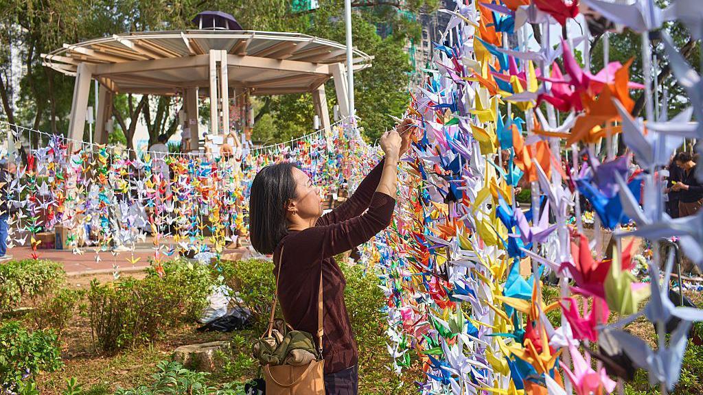 一位年輕女子正在製作摺紙花環，悼念火災罹難者。
