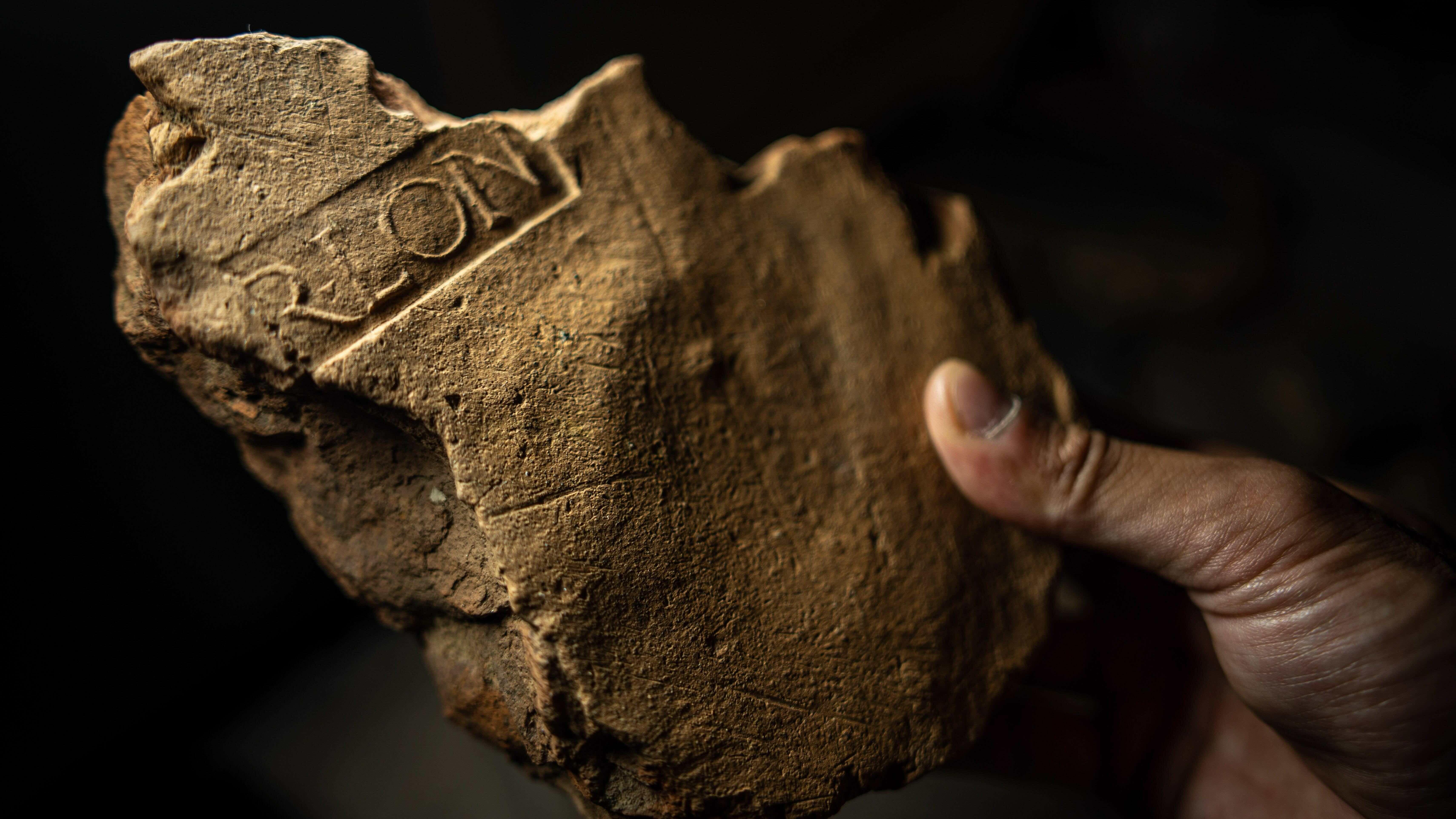 Un primer plano de un trozo roto de piedra de color marrón claro. Son claramente visibles los restos de algunas de las letras que quedaron impresas en el yeso al secarse: R-L-O-N. Significa Procurador de Londinium y muestra que el edificio del que formaba parte era un edificio civil en la ciudad en crecimiento.