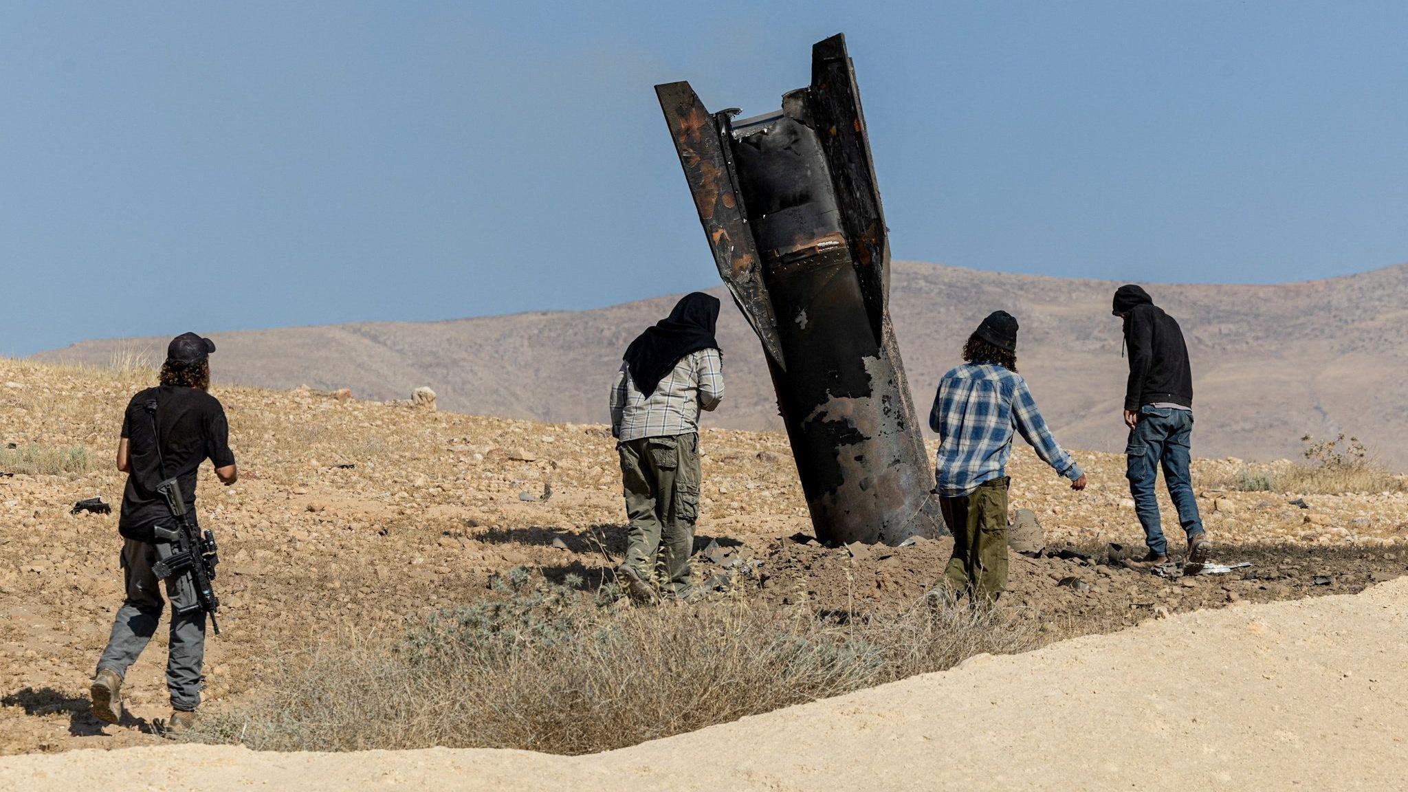 Parte de un misil lanzado sobresale del suelo en la zona de Cisjordania ocupada por Israel. Varias personas lo observan de cerca.