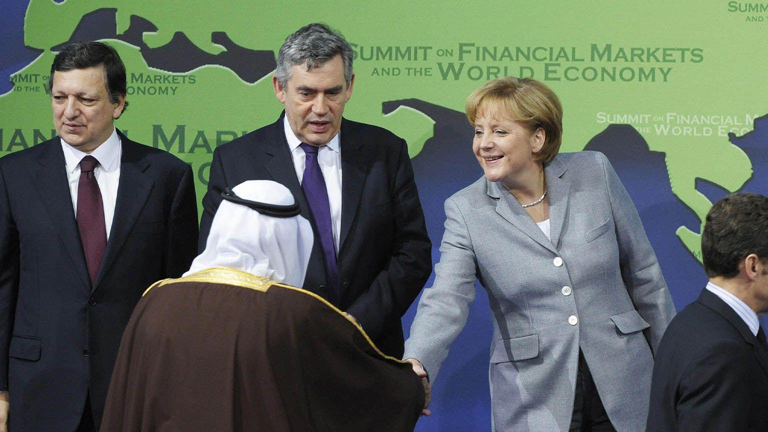 2008年11月15日，在華盛頓舉行的二十國集團峰會開幕式上，德國總理安格拉·默克爾（右二）與沙烏地阿拉伯國王阿卜杜拉握手，隨後他們與（從左到右）歐盟委員會主席若澤·曼努埃爾·巴羅佐、英國首相戈登·布朗和法國總統薩爾科齊一起拍攝大合照。
