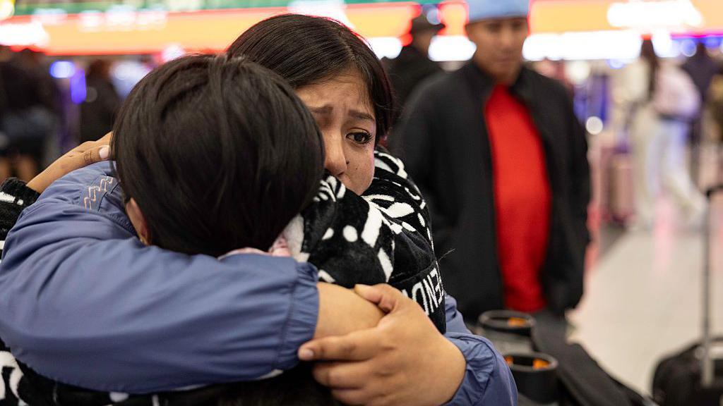 La inmigrante ecuatoriana Andrea, de 28 años, recibe un largo abrazo de su hermana (de frente a la cámara) antes de su vuelo a Ecuador en el Aeropuerto Internacional JFK el 26 de octubre de 2025 en Nueva York, Nueva York. Andrea y su prima decidieron “auto-deportarse” con sus hijos después de que sus esposos fueran detenidos por agentes del Servicio de Inmigración y Control de Aduanas de Estados Unidos (ICE) y luego deportados a Ecuador debido a su estatus indocumentado. La hija menor de Andrea, Shanell, de 7 meses, nació en Estados Unidos y es ciudadana estadounidense. (Foto de John Moore/Getty Images)