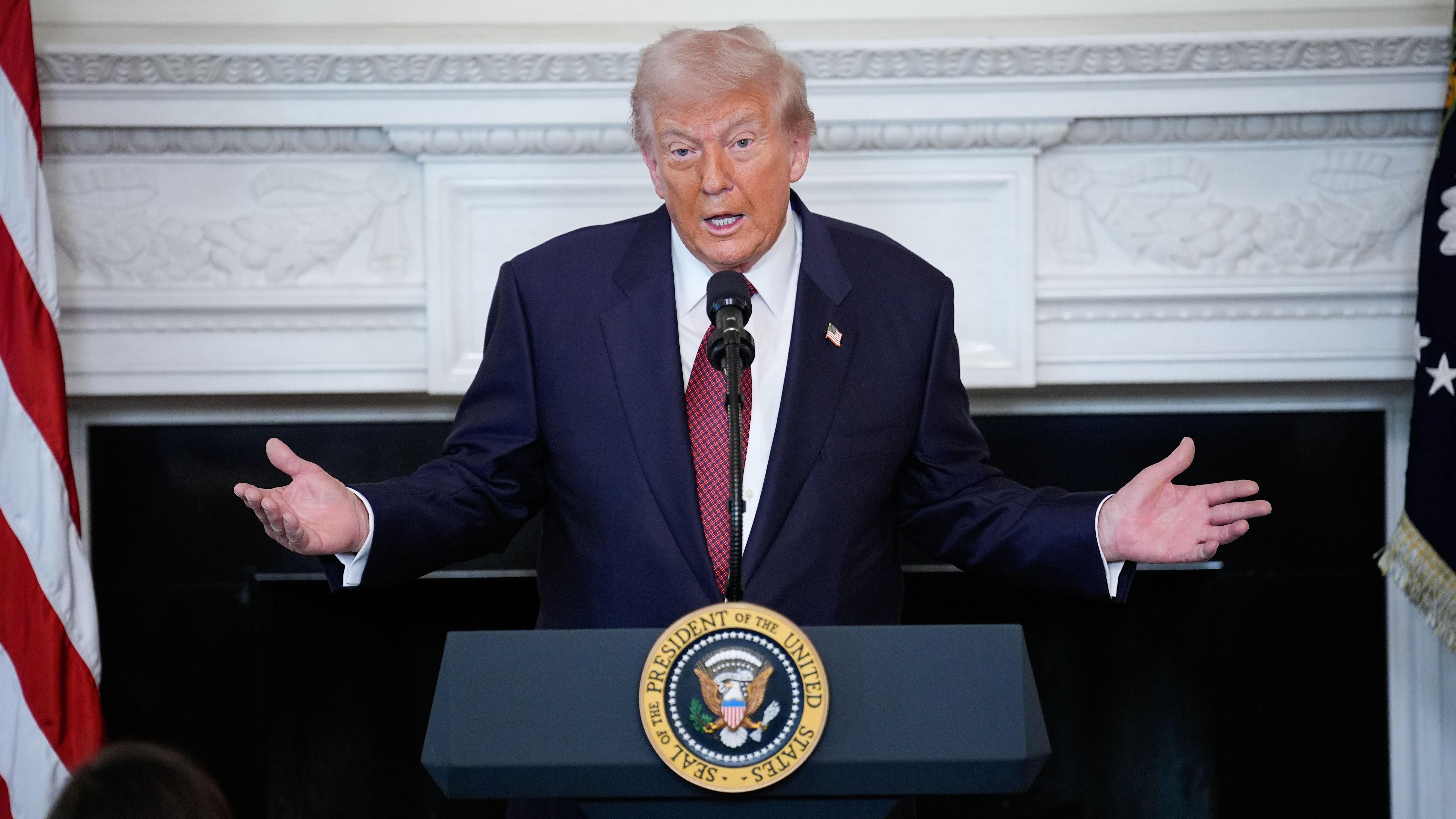 Donald Trump detrás de una atril gesticula con los brazos.