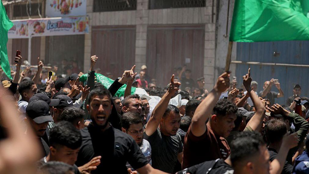 Los palestinos transportan los cuerpos de Imad Salim, también conocido como Abu Hassan, un alto mando del ala armada de Hamás, y de otras personas durante un cortejo fúnebre celebrado el mes pasado en la ciudad de Gaza. Los hombres vestidos de negro señalan al cielo, mientras que otros agitan banderas verdes.