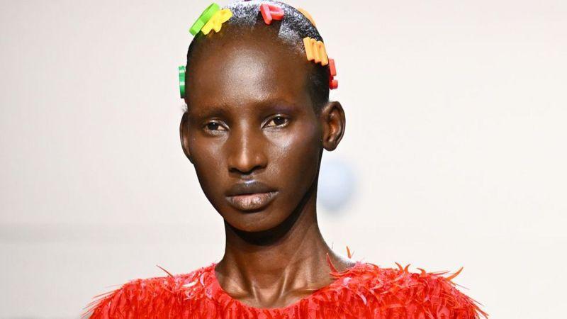 A modelo sul-sudanesa Arop Akol, de cabelo preso enfeitado com letras do alfabeto e blusa vermelha