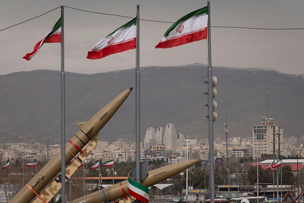 Dois m&iacute;sseis bal&iacute;sticos de fabrica&ccedil;&atilde;o iraniana ao lado de bandeiras do pa&iacute;s, com Teer&atilde; vis&iacute;vel ao fundo