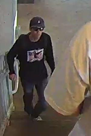 Un hombre delgado con gafas de sol, una gorra de béisbol oscura y un suéter oscuro con una imagen de la bandera estadounidense en la parte delantera subiendo por una escalera