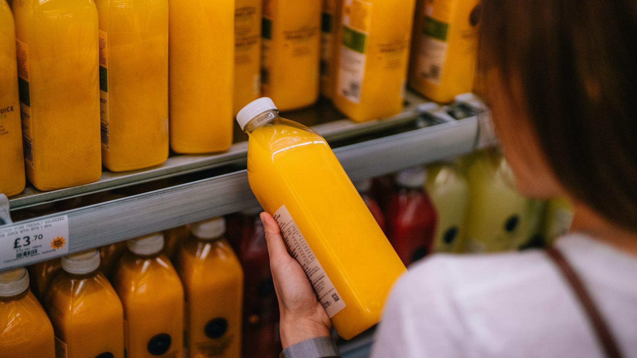 Mujer leyendo la etiqueta de un jugo de naranja en un supermercado. 