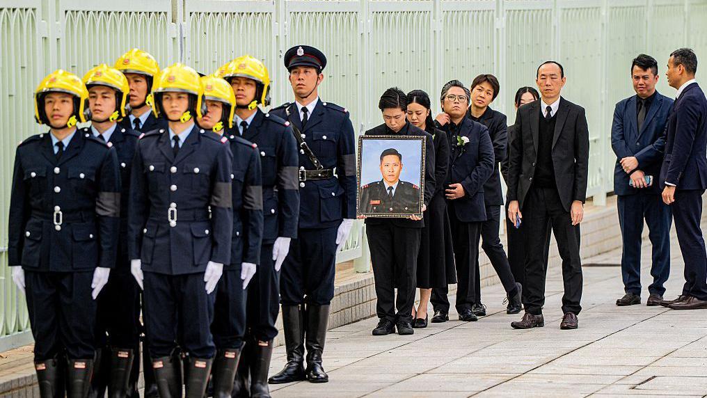 Relatives of firefighter Ho Wai-ho, who died in the deadly fire at the Wang Fuk Court residential estate in Tai Po district, hold his portrait during his burial at Gallant Garden in Hong Kong on December 19, 2025. 