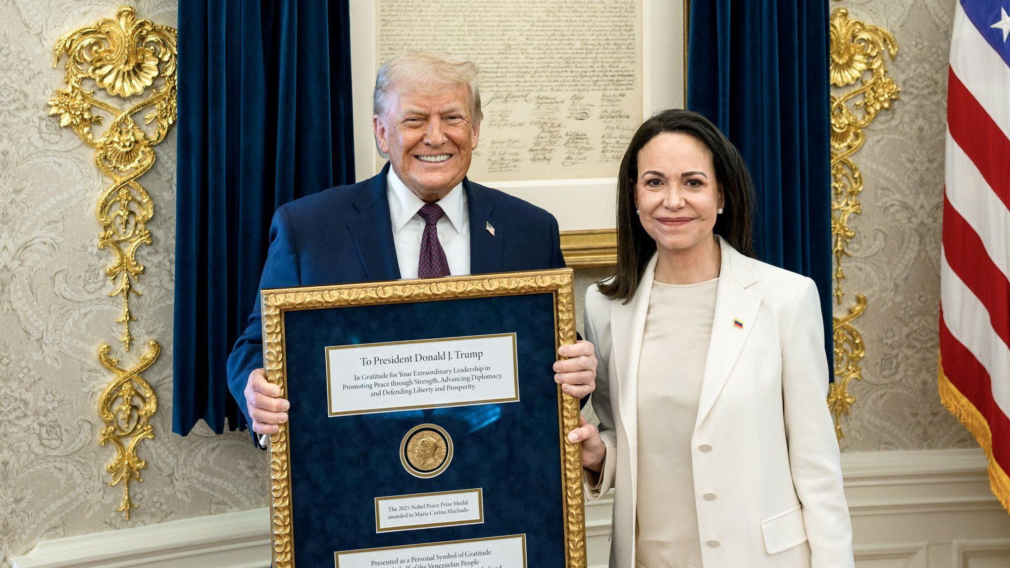 Donald Trump sonríe y sostiene un cuadro en el que está la medalla del Nobel de Paz recibido por María Corina Machado, mientras posa junto a la líder venezolana en la Casa Blanca.