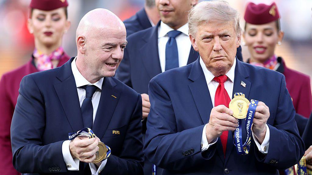 O presidente da Fifa, Gianni Infantino, aplaude enquanto fala e segura medalhas  de vencedores durante a apresenta&ccedil;&atilde;o do trof&eacute;u na final da Copa do Mundo de 2026, entre Espanha e Argentina, no Est&aacute;dio MetLife em Nova York, ao lado do presidente americano, Donald Trump