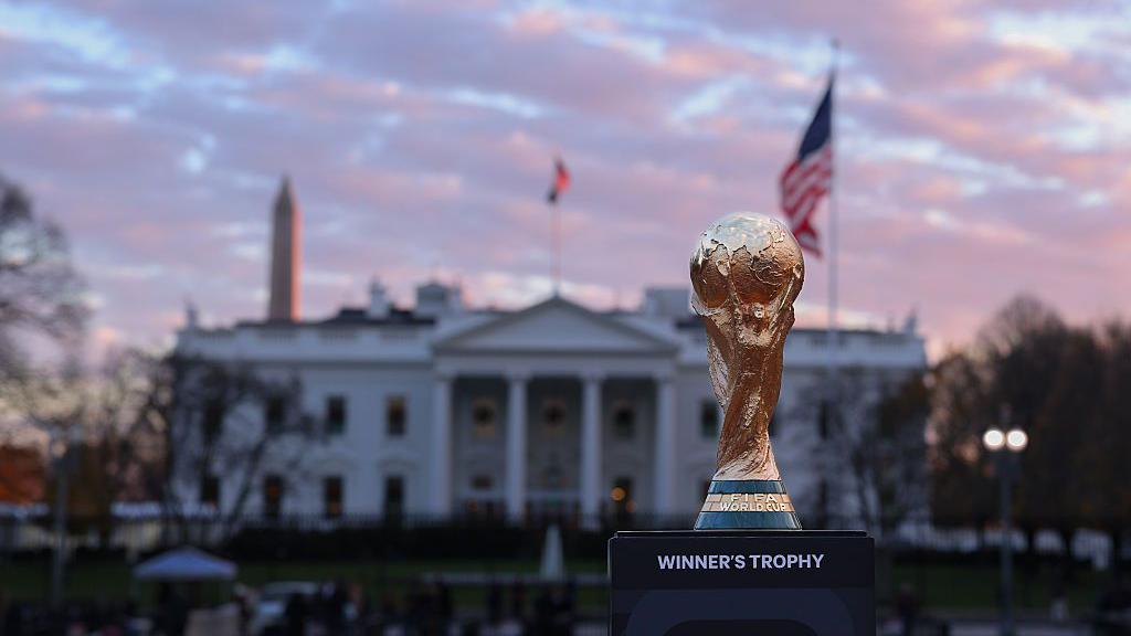 El trofeo de la Copa del Mundo se encuentra frente a la Casa Blanca, flanqueado a ambos lados por una bandera de los Estados Unidos y el Monumento a Washington.