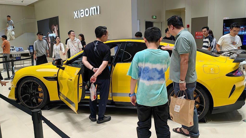 Un automóvil amarillo en un centro comercial está rodeado de personas. El el fondo, un letrero de Xiaomi