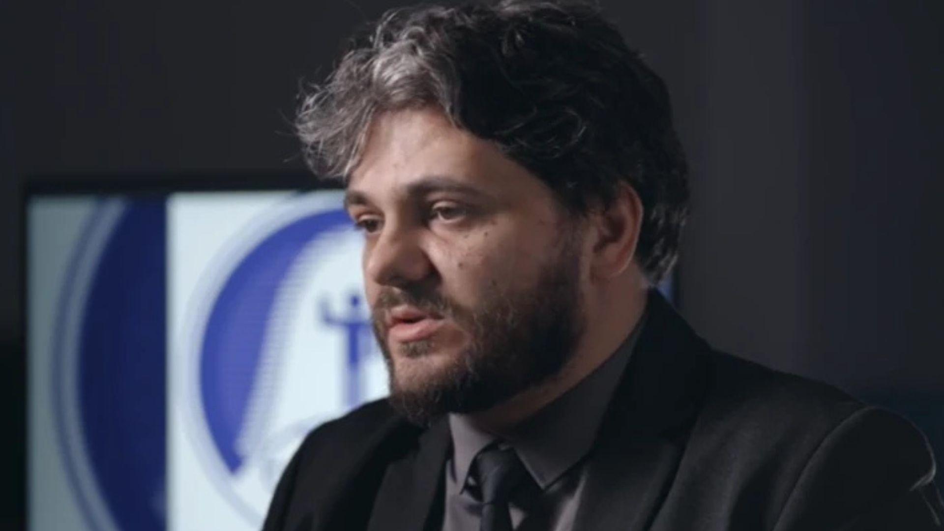 Muškarac u crnom odelu i crnoj košulji sedi