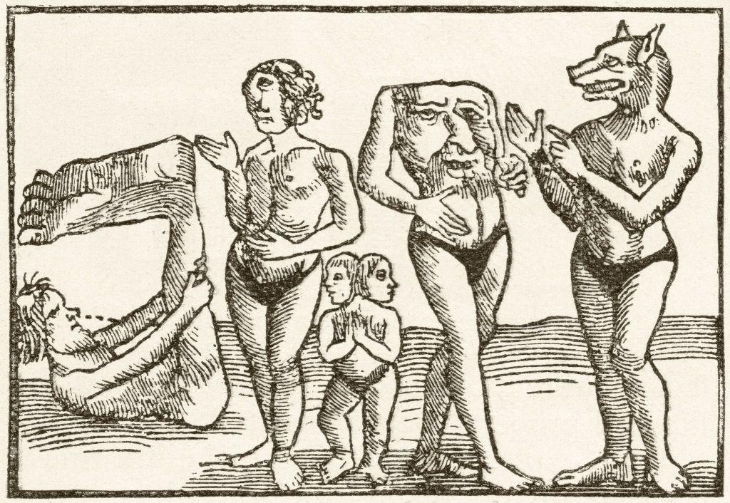 A imagem mostra uma gravura antiga em preto e branco retratando seres fant&aacute;sticos com caracter&iacute;sticas h&iacute;bridas entre humanos e animais. Entre as figuras aparecem uma criatura com cabe&ccedil;a de c&atilde;o, outra com rosto no tronco, uma pessoa sem cabe&ccedil;a e outra com duas cabe&ccedil;as, al&eacute;m de um homem contorcido &agrave; esquerda. A ilustra&ccedil;&atilde;o remete &agrave;s representa&ccedil;&otilde;es medievais de povos considerados 