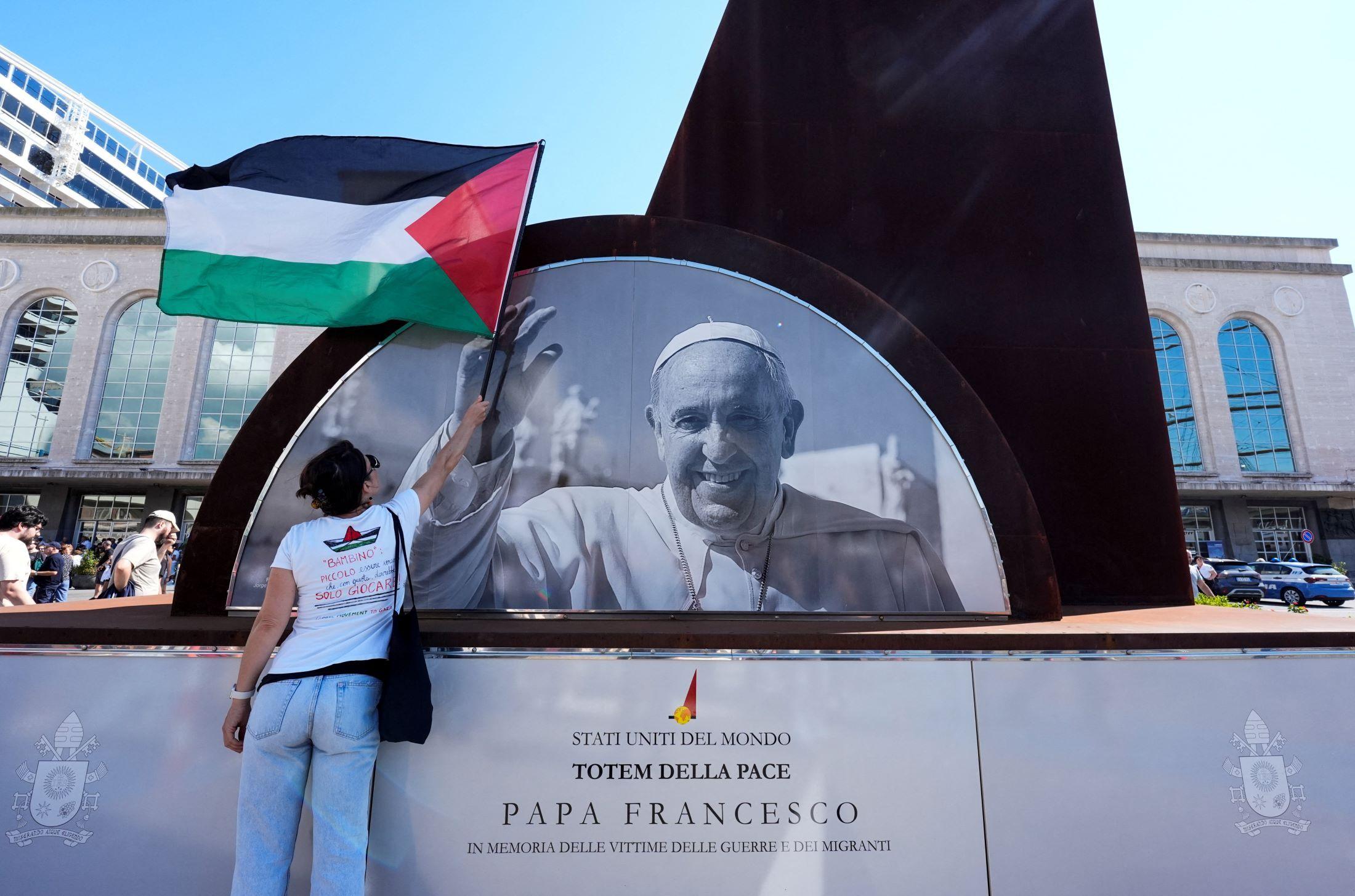 Una persona ondea una bandera palestina ante un monumento de recuerdo al papa Francisco en Nápoles, Italia.