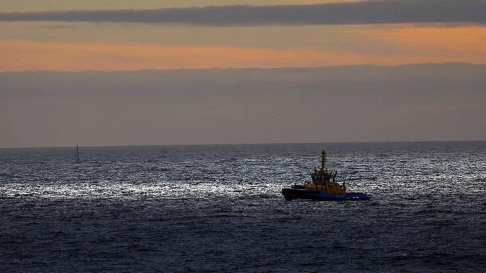 Un barco en el mar con el cielo gris azulado y rosado 